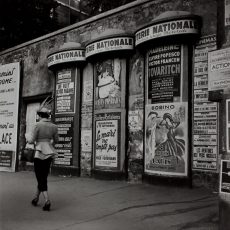 Habillée d&rsquo;un tailleur trotteur, passant devant les colonnes Morris du quartier de l&rsquo;Opéra, une femme chic