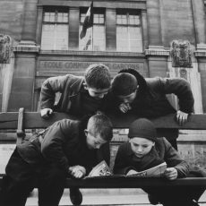 Quatre jeunes garçons lisant le « Journal de Mickey », devant une école communale de garçons