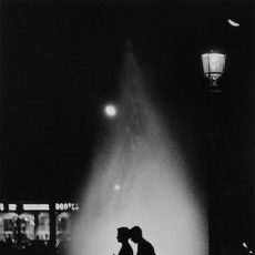 De nuit, un couple passe devant les fontaines illuminées du rond-point des Champs-Élysées